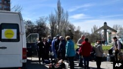 People wait to board a bus during their evacuation, with a MiG-17 fighter jet monument in the background, in Kramatorsk, Ukraine, April 9, 2022.