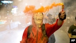 A protester wearing a mask holds a firework during a rally outside the headquarters of the Siam Commercial Bank, a publicly-held company in which the Thai king is the biggest shareholder, in Bangkok Thailand, Nov. 25, 2020.