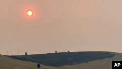 Smoke obscures the air and dims the sun over a hillside burned by a recent wildfire, in Missoula, Mont., on Sunday, July 18, 2021. Extreme heat descended on parts of the U.S. northern Rocky Mountains on Monday, July 19 as authorities struggled to…