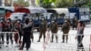 Armed police and soldiers stand guard behind a road barricade with razor wire in Mandalay, Myanmar Friday, Feb. 19, 2021. A young woman who was shot in the head by police during a protest last week against the military's takeover of power in Myanmar died Friday morning, her broth